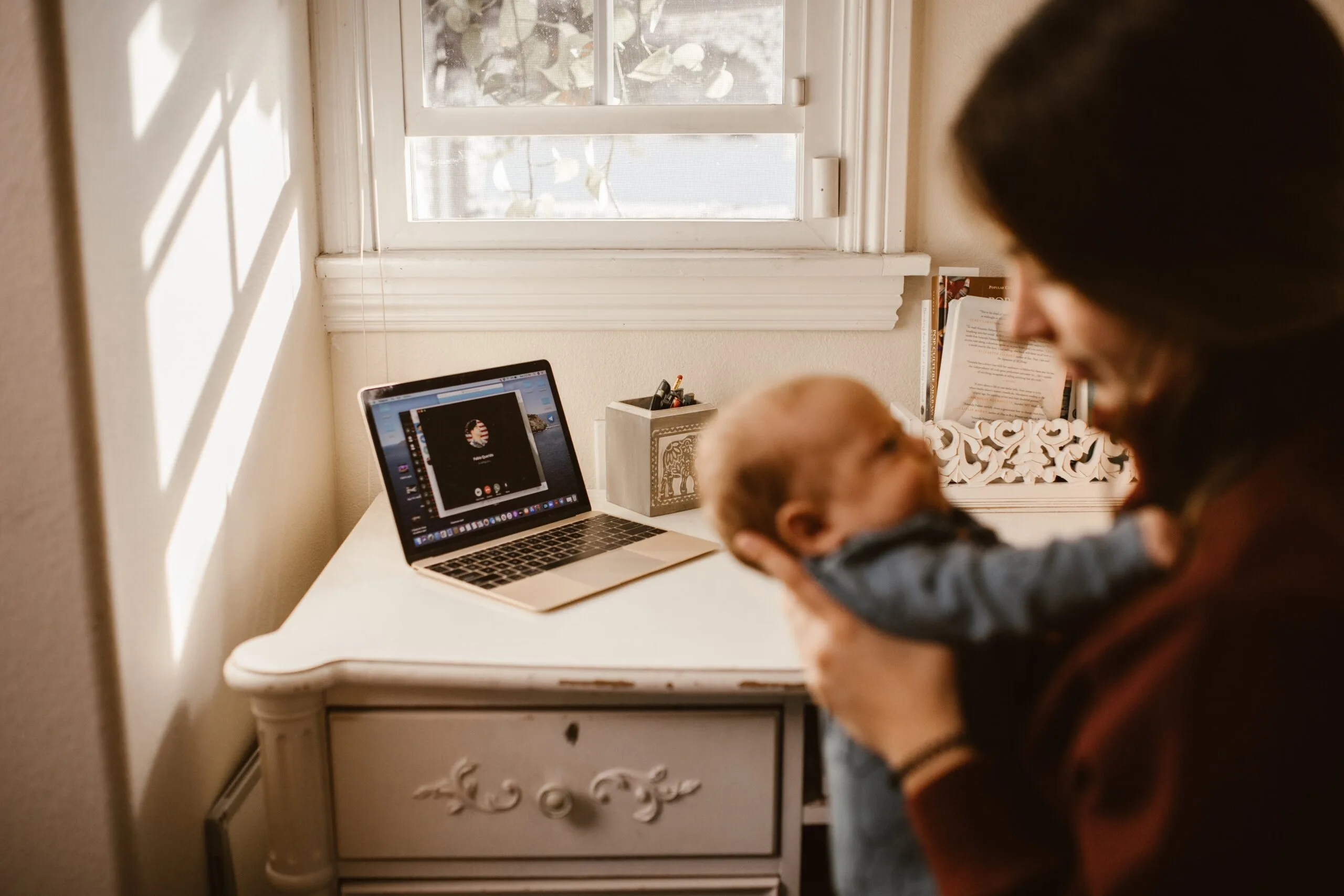 Mulher segura bebê com notebook ao fundo
