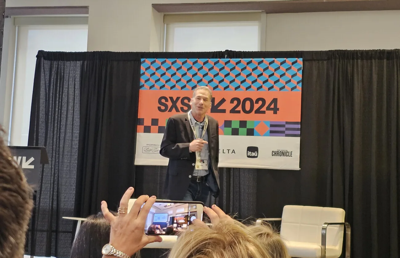 Man presenting at SXSW 2024 event with audience member capturing photo on smartphone.