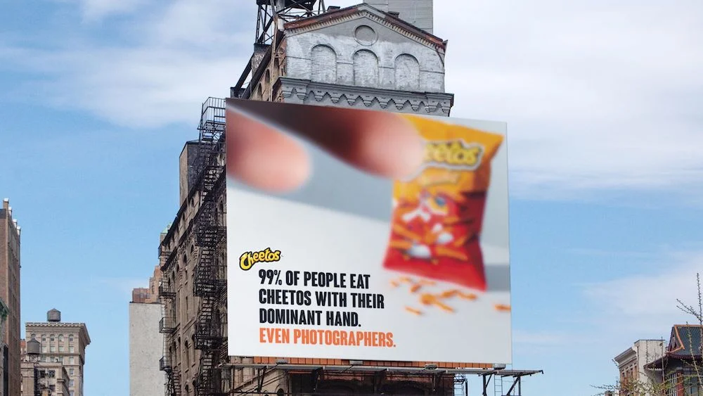 Person holding a Cheetos pack with a billboard in the background displaying a fun fact about people eating Cheetos with their dominant hand.