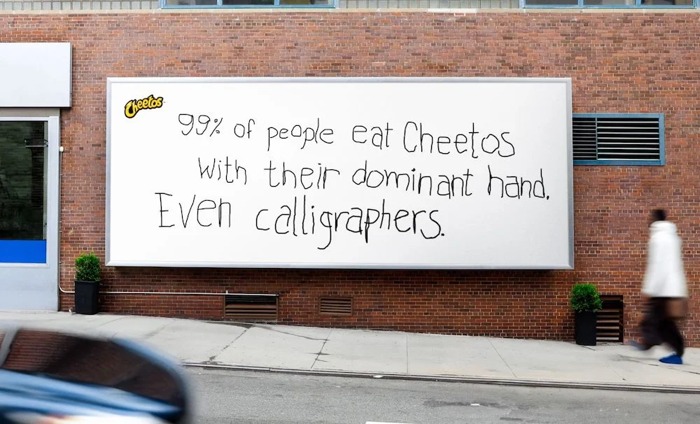 Cheetos billboard advertisement with interesting fact about people eating snacks with their dominant hand, displayed on a city street.