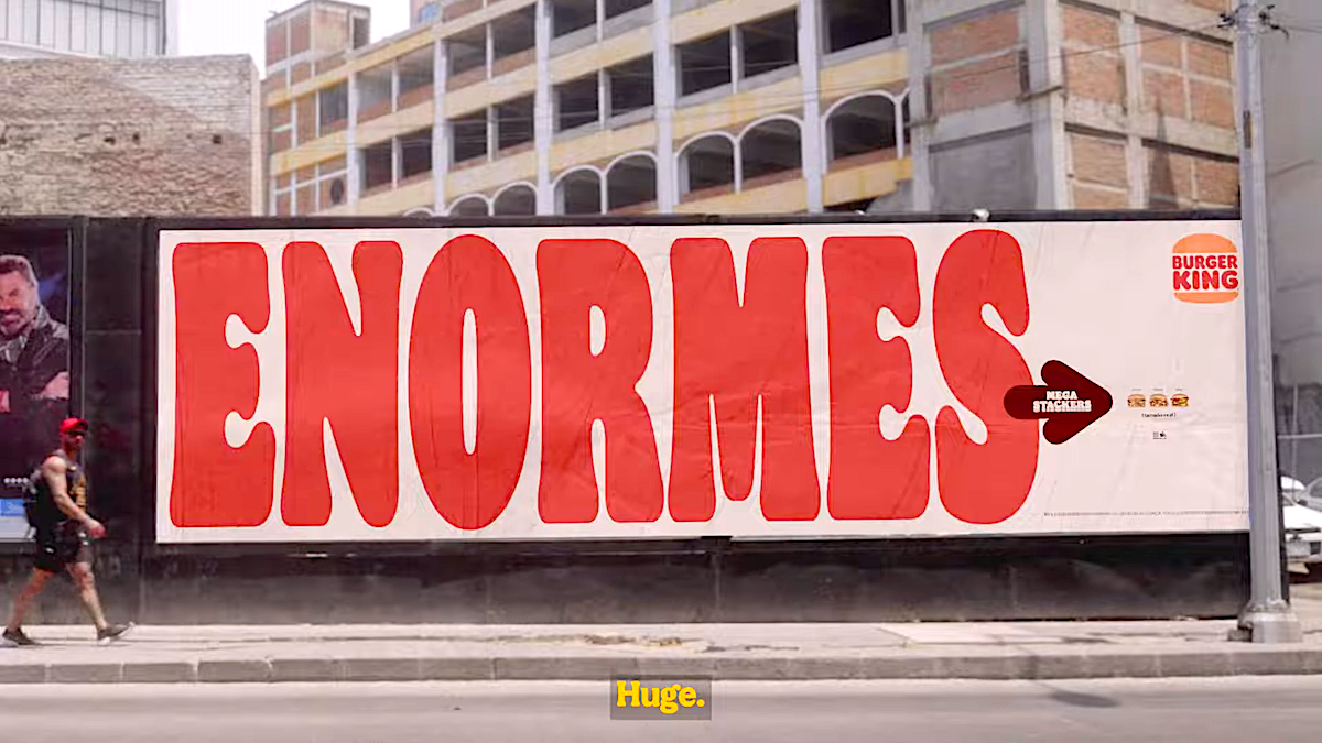 Burger King billboard advertising Mega Stacker burgers with large text "ENORMES" on city street.