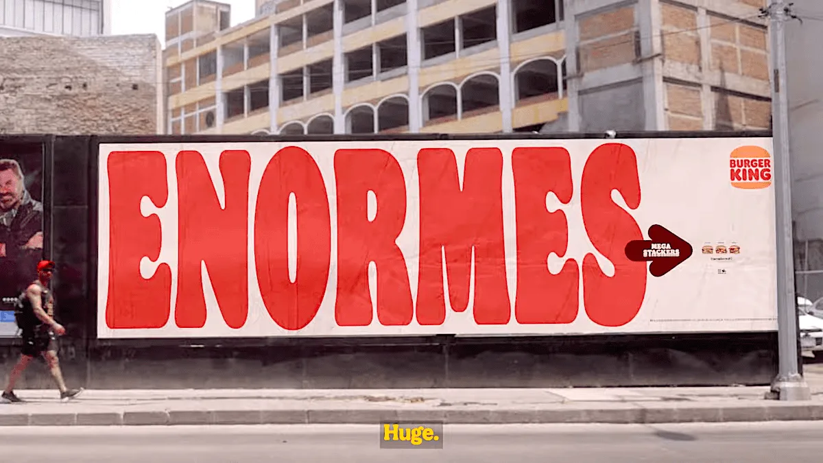 Burger King billboard advertising Mega Stacker burgers with large text "ENORMES" on city street.