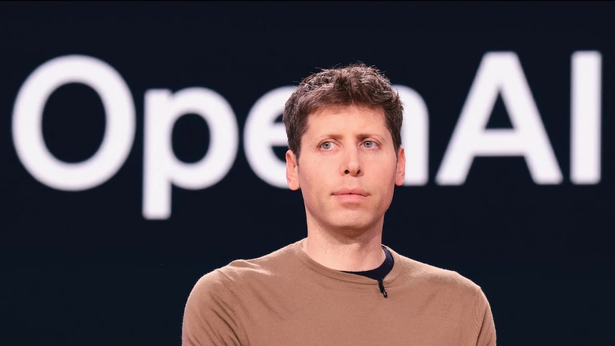 Man speaking at OpenAI event with logo in background