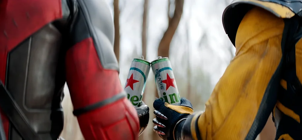 Two people in superhero costumes toasting with Heineken Silver cans in an outdoor setting