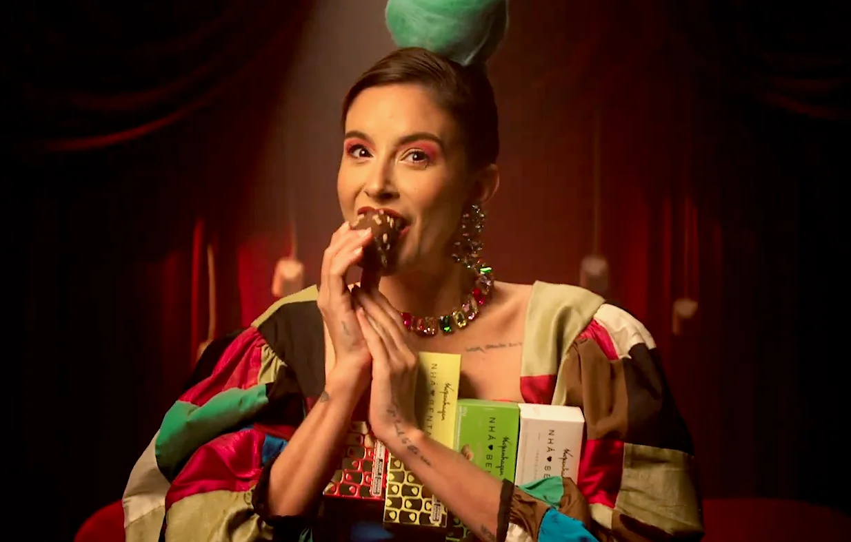 Woman enjoying chocolate bar while holding assorted chocolate boxes in colorful attire