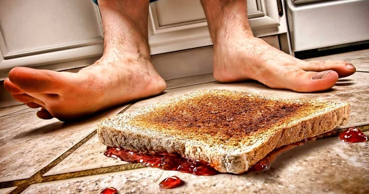 Person standing near a dropped sandwich with jelly on a tiled kitchen floor.