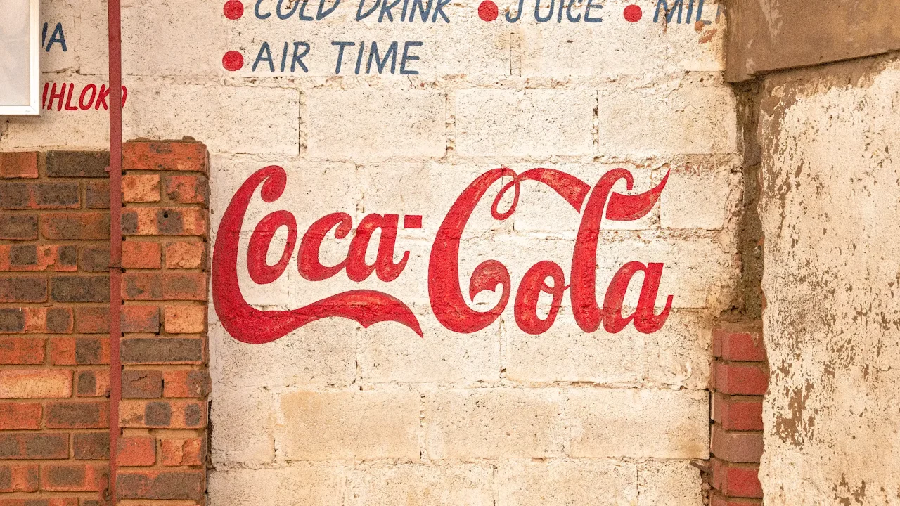 Vintage Coca-Cola wall advertisement on a brick and plaster surface.