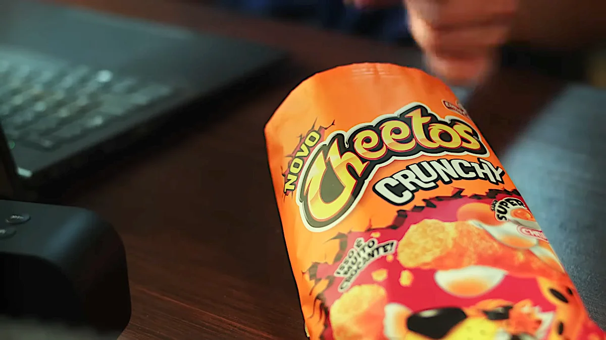 Bag of Cheetos Crunchy snacks on a wooden table near a laptop.