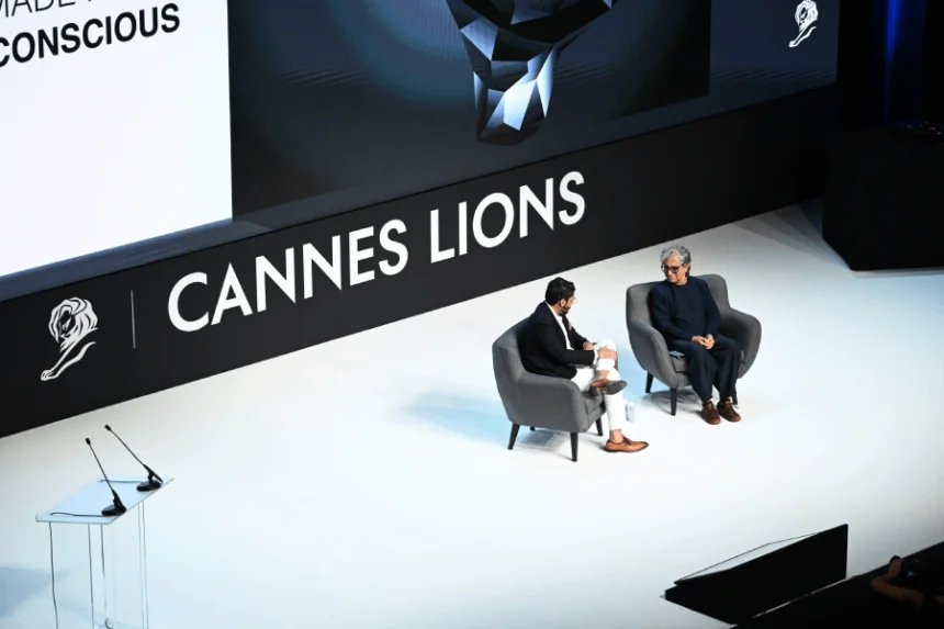Deepak Chopra. Two speakers on stage at Cannes Lions event, seated in chairs, discussing in front of a large screen.