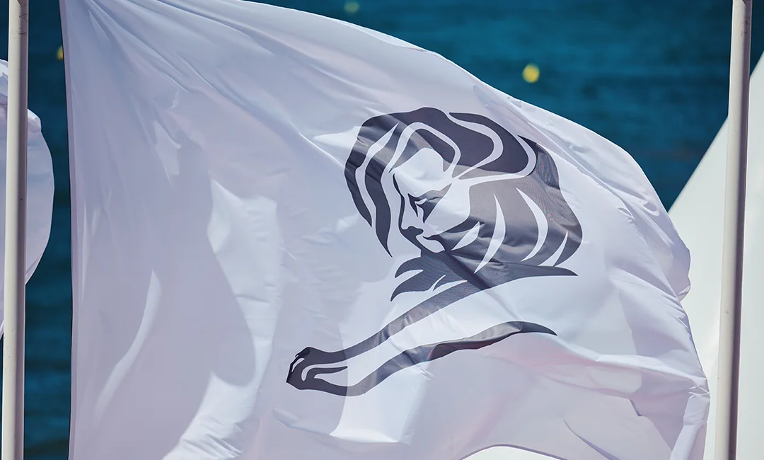 White flag with a black lion logo waving against a blue sky background.