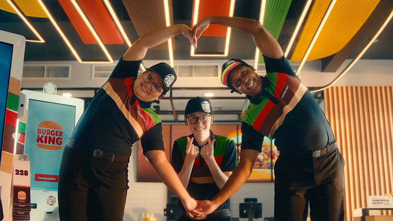 Burger King employees forming a heart shape with their arms, smiling and posing inside a brightly lit restaurant.