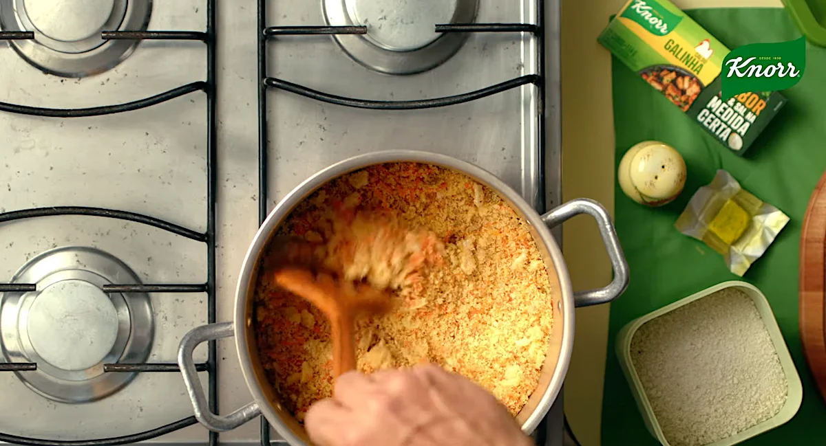 Cooking rice with Knorr seasoning on a stovetop, wooden spoon stirring, ingredients and Knorr packaging visible.