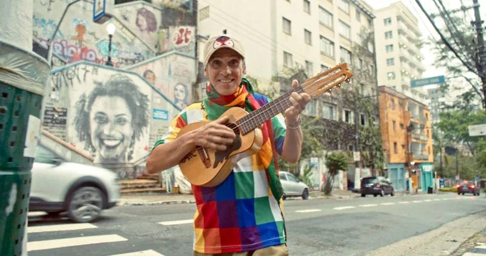 Street musician playing guitar in colorful shirt on urban street with graffiti in the background