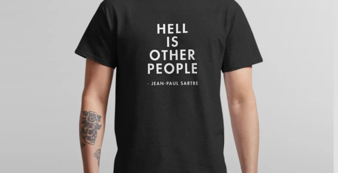 Man wearing black t-shirt with "Hell is Other People" quote by Jean-Paul Sartre, visible tattoo on left arm.