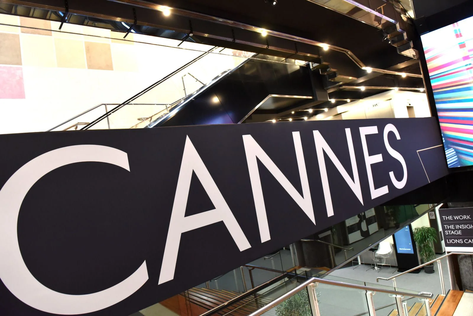 Cannes sign inside a modern building with escalators and colorful displays.