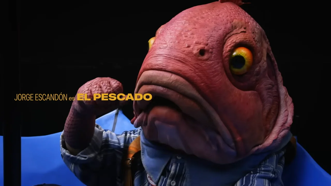 Suerte. Large fish-headed character in a plaid shirt with text "Jorge Escandón es El Pescado" on a dark background.