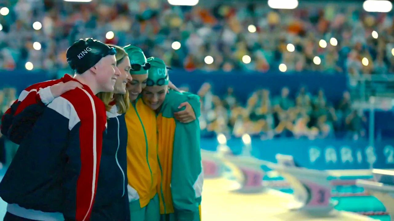 Swimmers celebrating after a race at a swimming competition with a cheering crowd in the background.