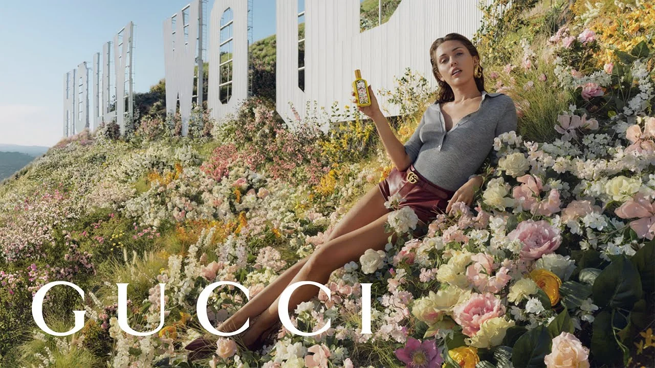 Gucci perfume advertisement featuring a woman in a floral field near the Hollywood sign.