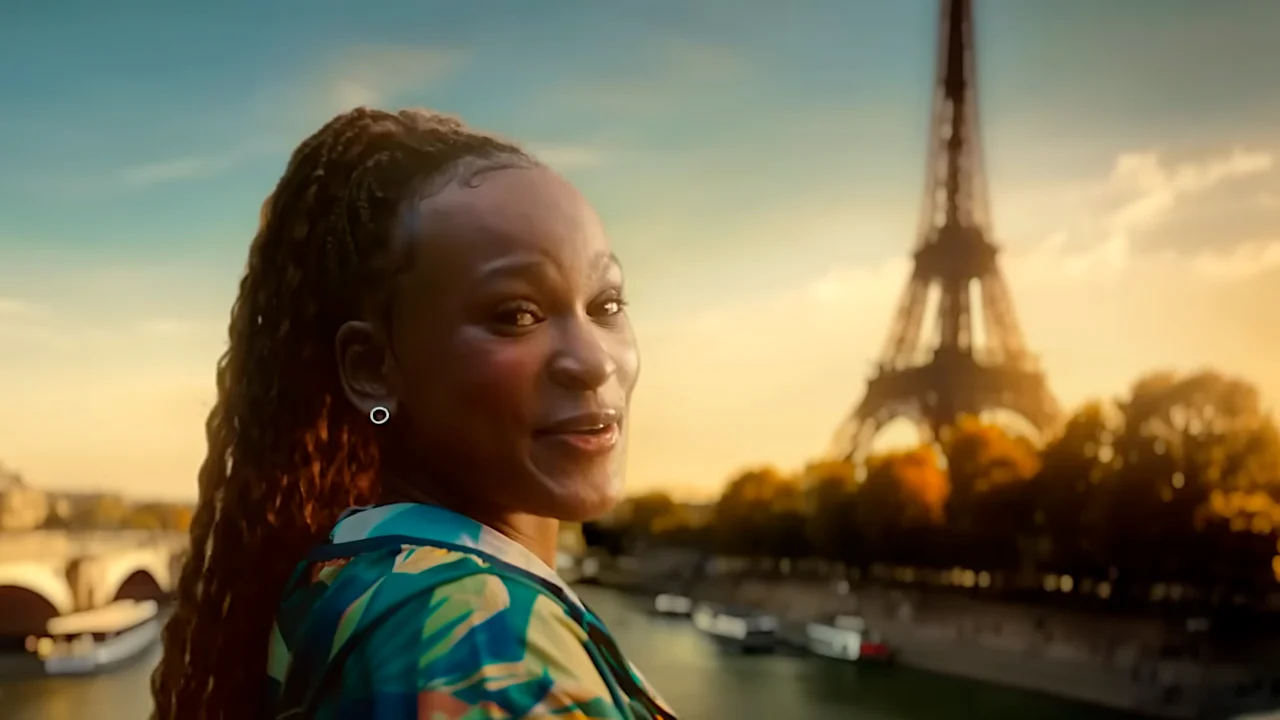 A smiling woman with curly hair poses in front of the Eiffel Tower during sunset, showcasing a vibrant cityscape along the Seine River in Paris, France.