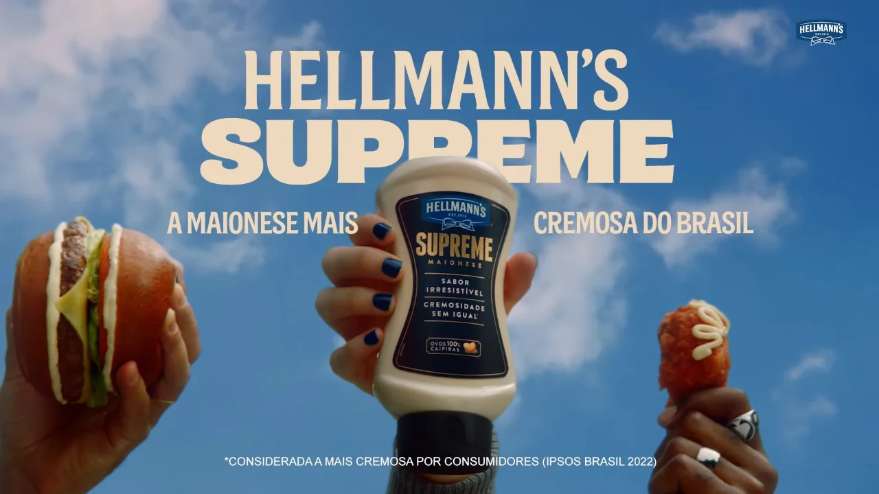 Hellmann's Supreme mayonnaise bottle held between a sandwich and a fried snack, with text highlighting its creaminess and popularity in Brazil.