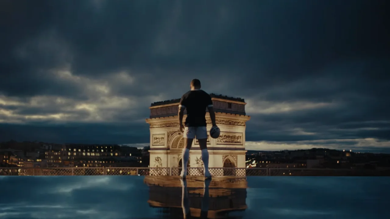 Rugby player standing in front of Arc de Triomphe at night, Paris skyline in background