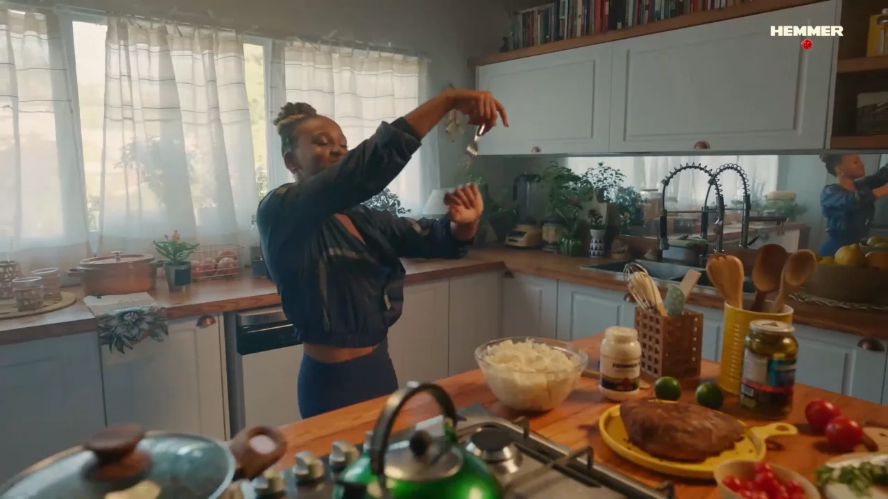 Woman seasoning food in a cozy kitchen with natural light and wooden countertops.