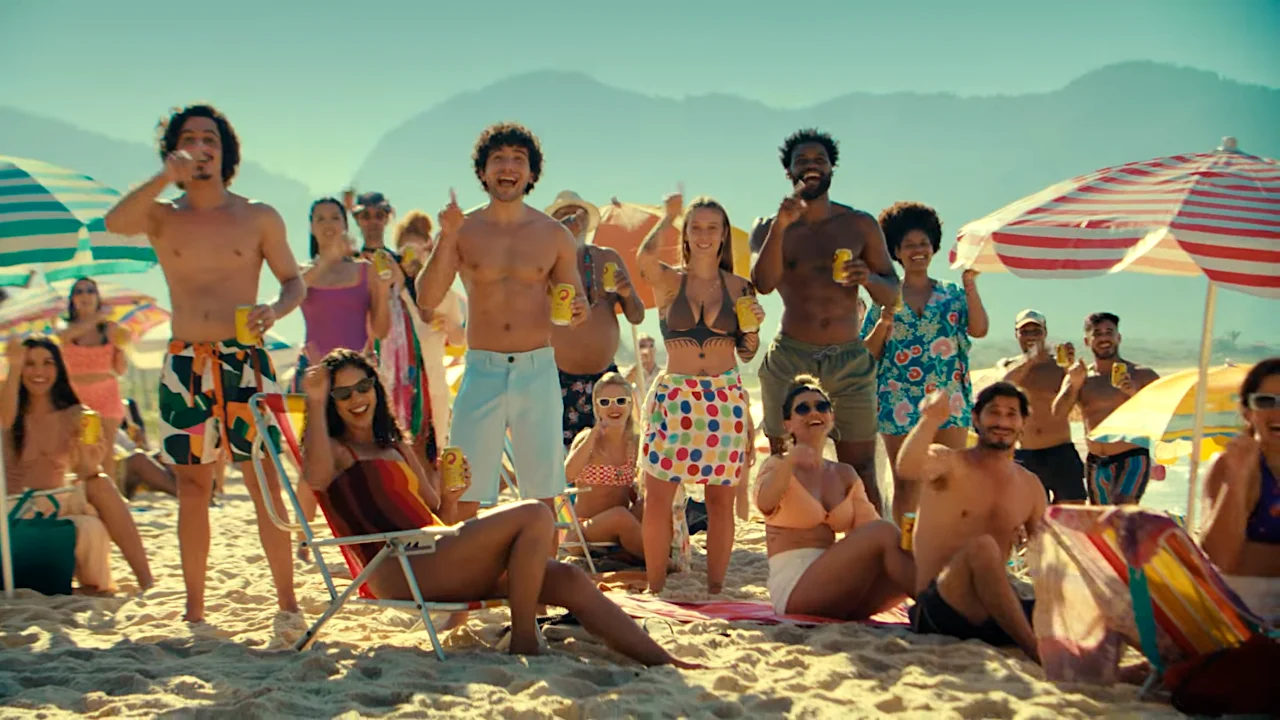 Group of people enjoying a sunny day at the beach with drinks, umbrellas, and beachwear.