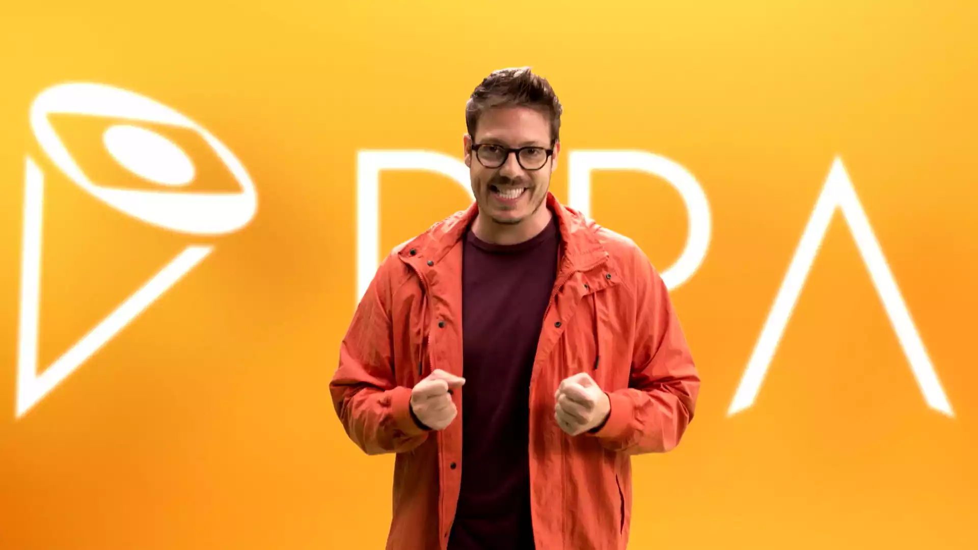 Man in orange jacket smiling with enthusiasm in front of a bright yellow background with a logo and the letters "DPA".