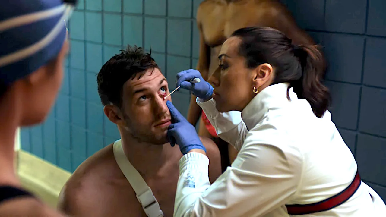 A medical professional wearing gloves examines a male athlete's eye in a locker room setting, emphasizing sports medicine and athlete care.