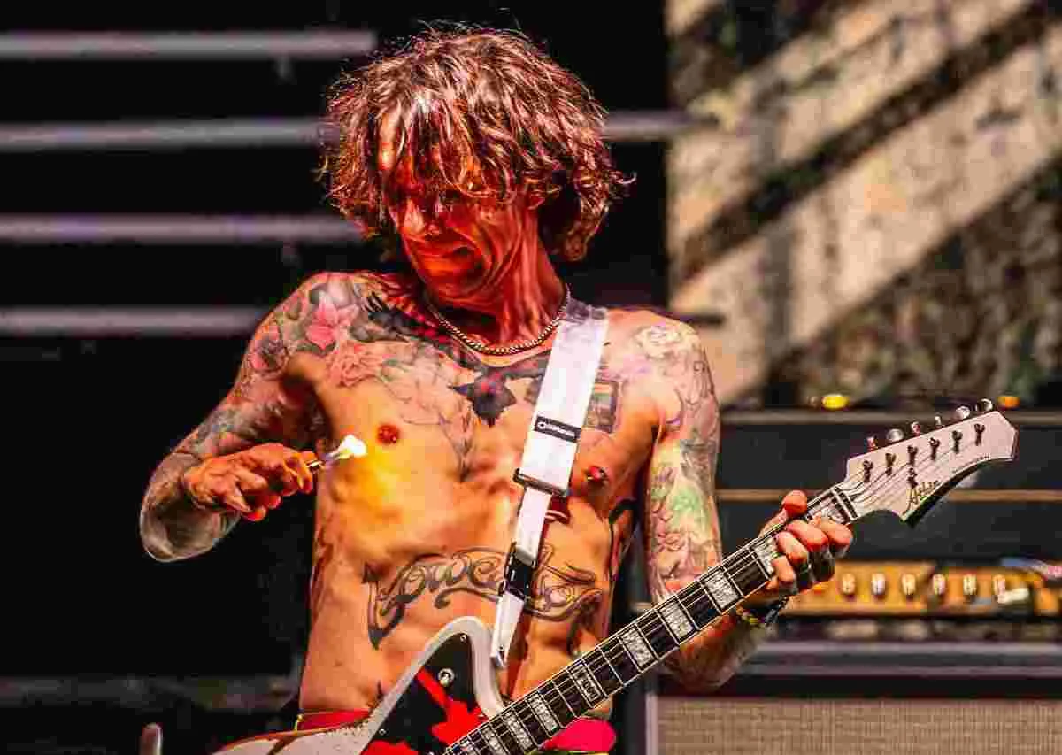 Guitarrista tatuado com guitarra em apresentação ao vivo.