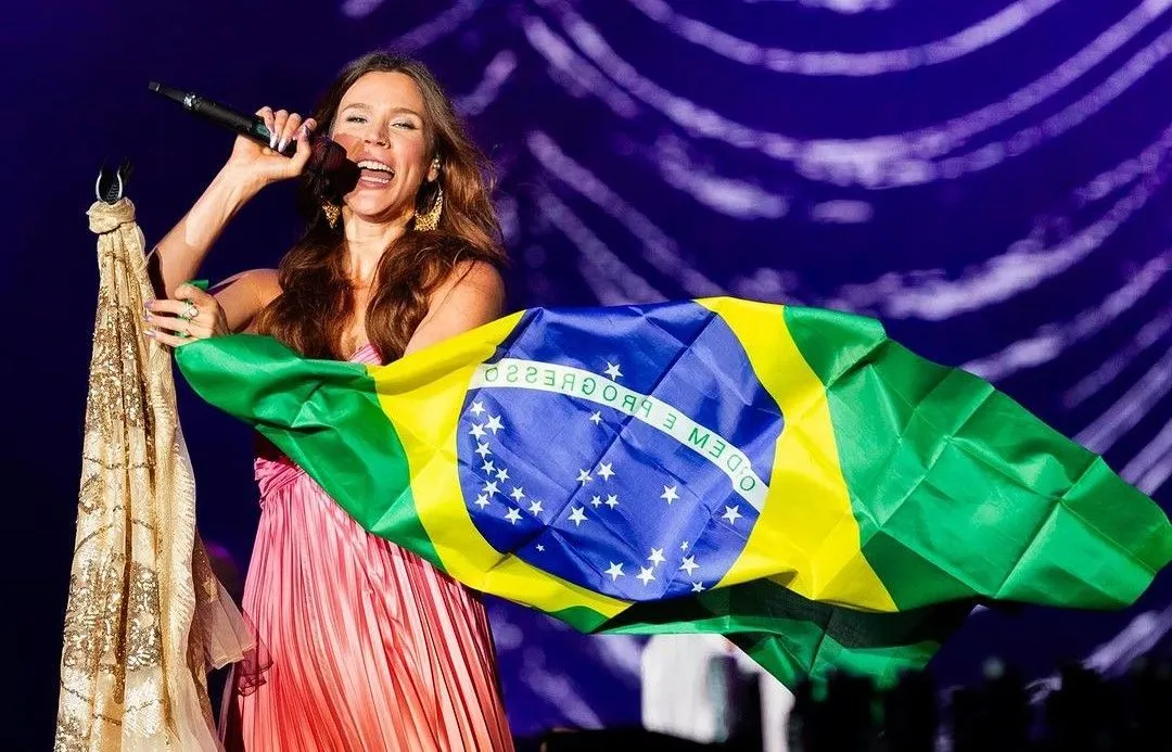 Cantora segurando bandeira do Brasil no palco.