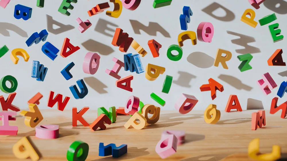 Letras coloridas espalhadas sobre a mesa de madeira.