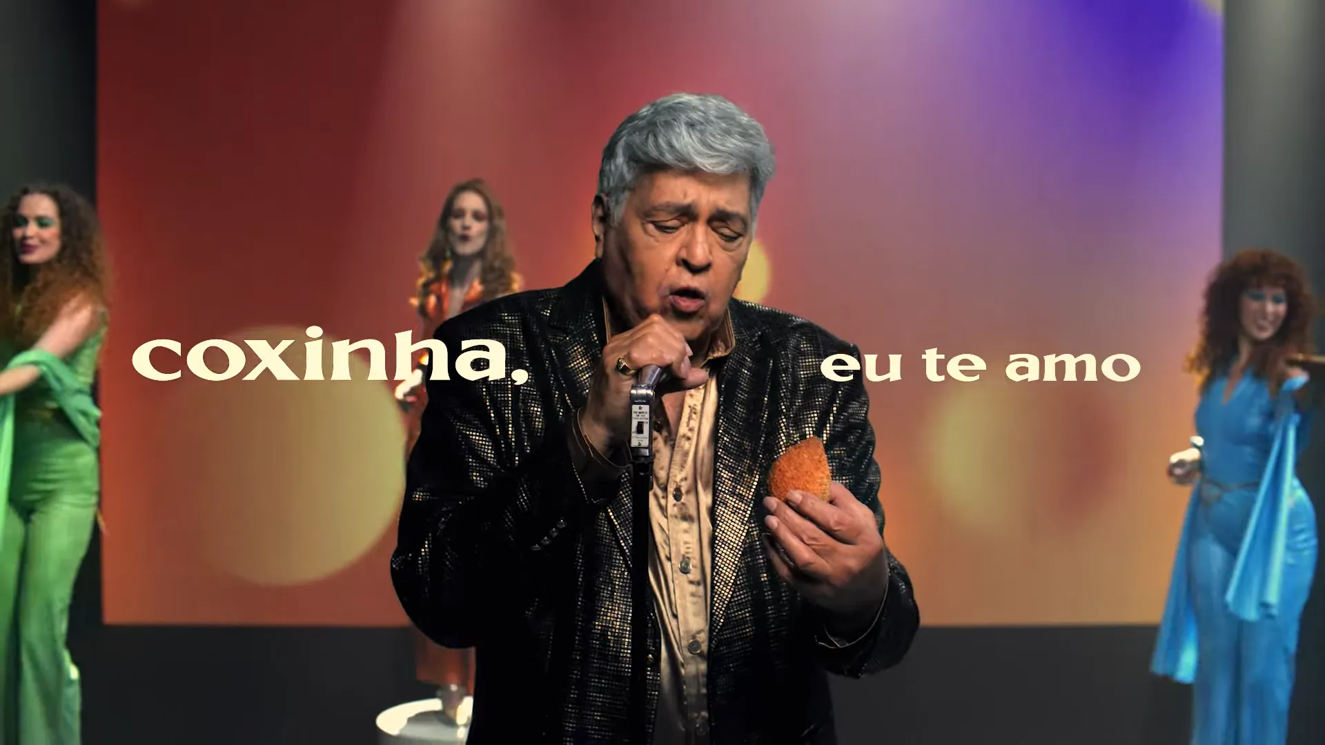 Cantor segurando coxinha no palco, letras grandes.