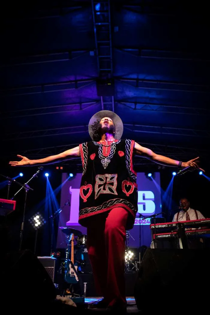 Cantor performa em palco iluminado com braços abertos.