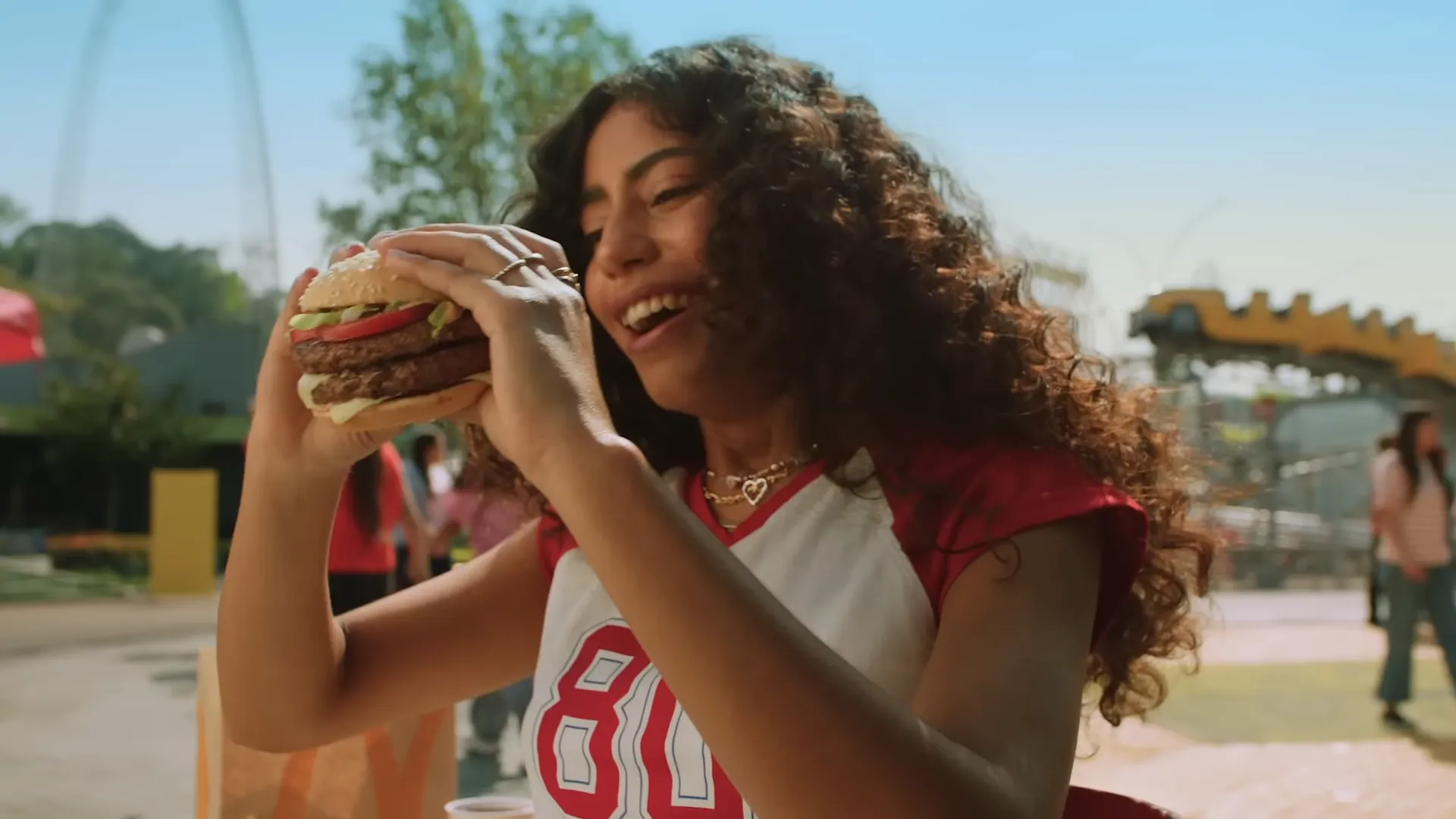 Pessoa alegre comendo hambúrguer em parque de diversões.