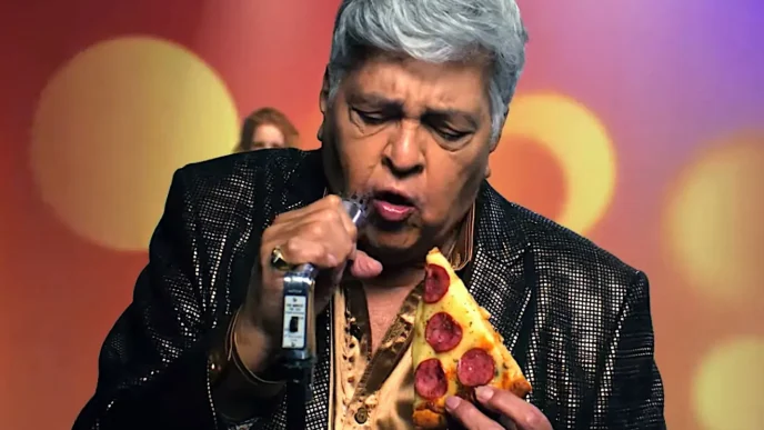 Homem canta segurando pizza e microfone.