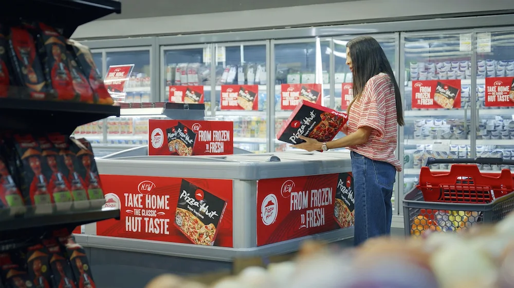 Mulher escolhendo pizza congelada em supermercado.