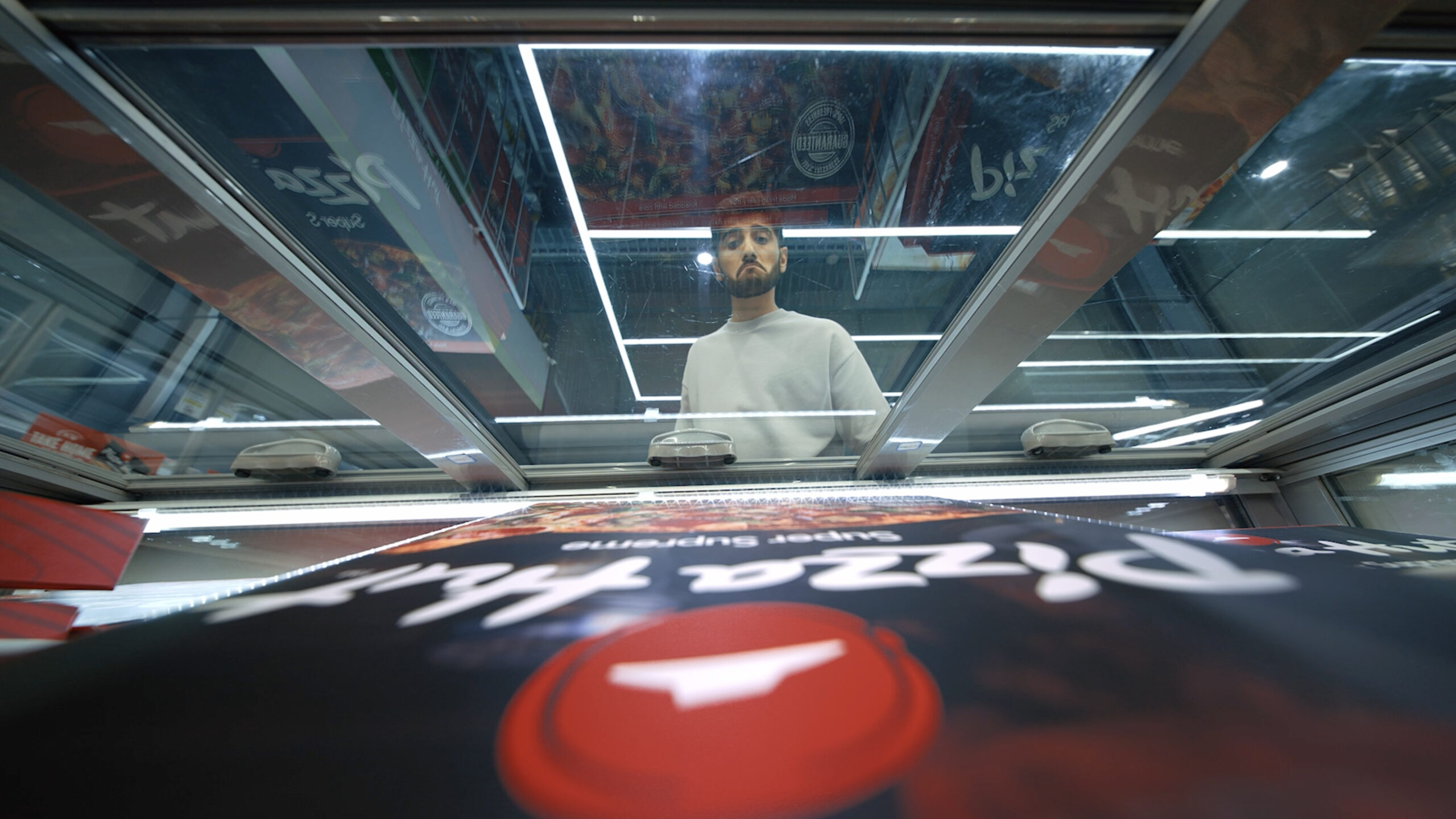 Homem olhando pizza congelada no freezer de supermercado.