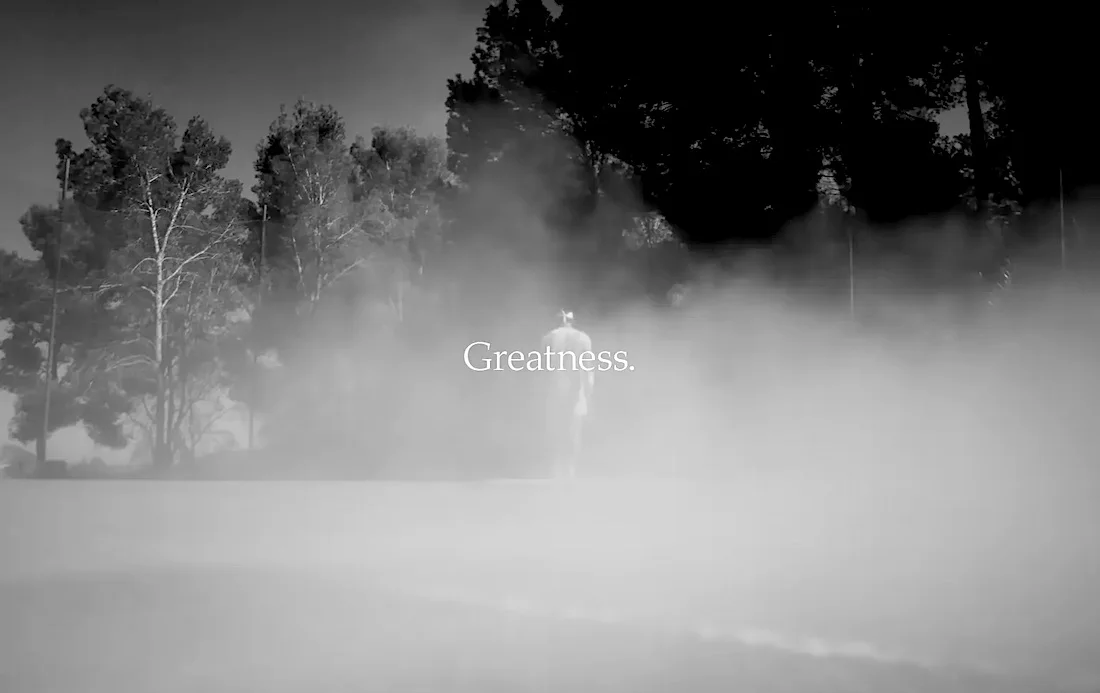 Pessoa caminhando em campo enevoado, texto 'Greatness'.