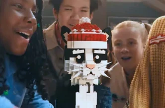 Crianças admirando gato de LEGO com touca vermelha.