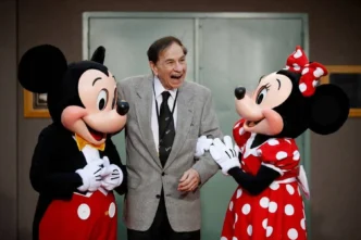 Homem sorrindo entre Mickey e Minnie Mouse.