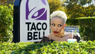 Mulher com bebida ao lado de placa Taco Bell.