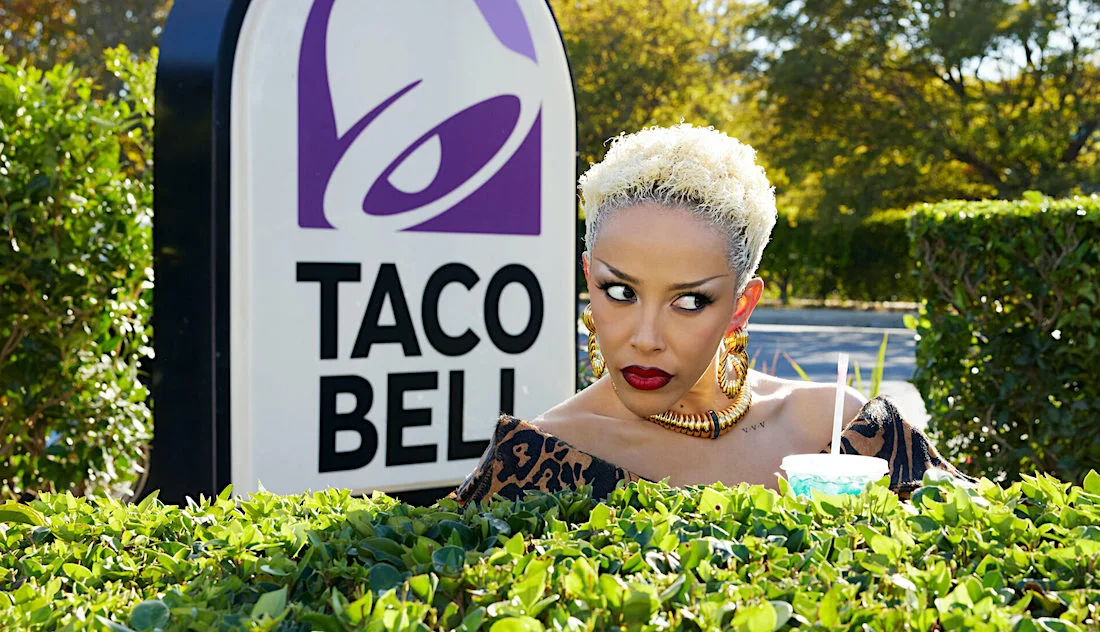 Mulher com bebida ao lado de placa Taco Bell.