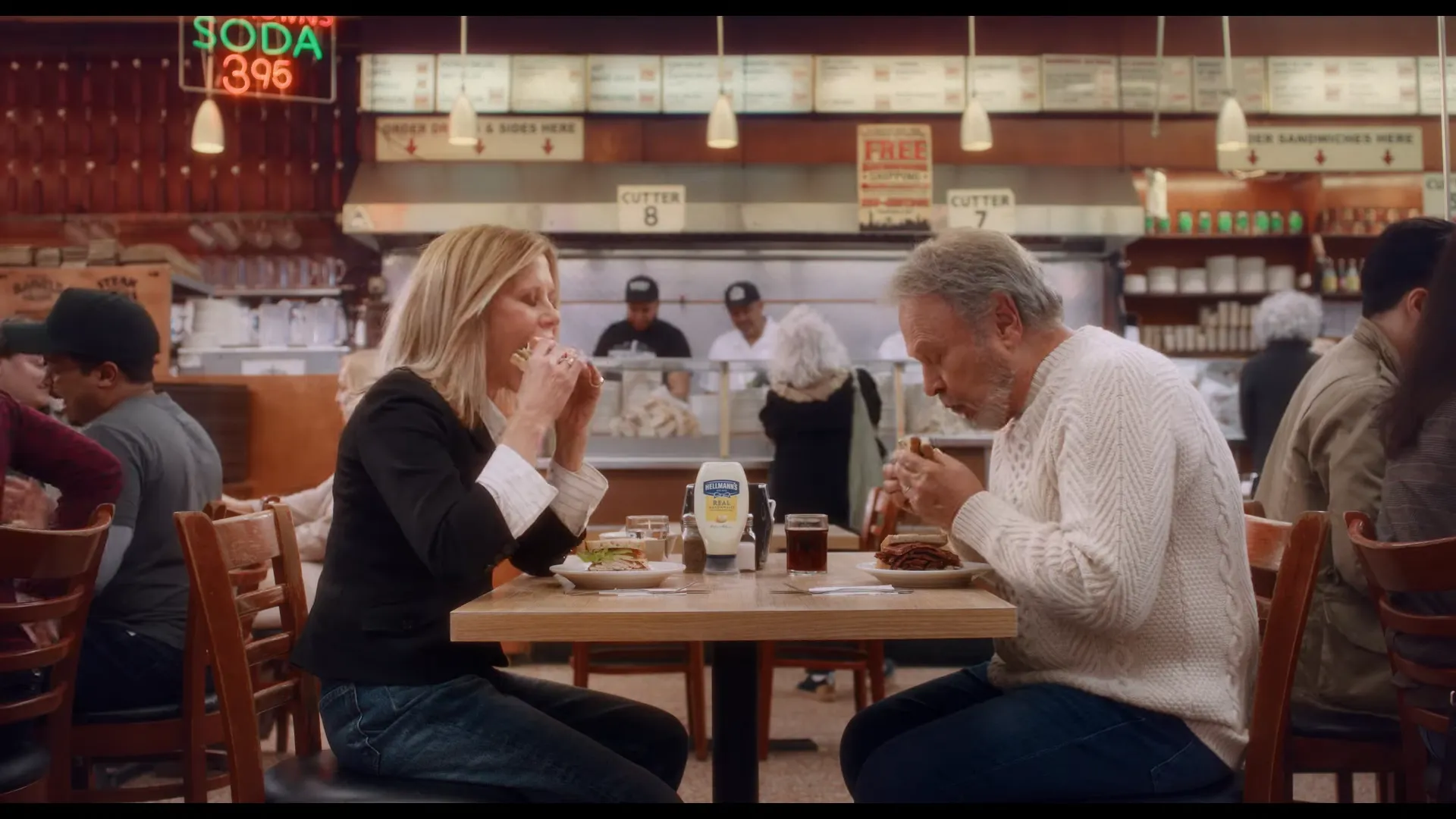 Casal comendo sanduíche em restaurante movimentado.