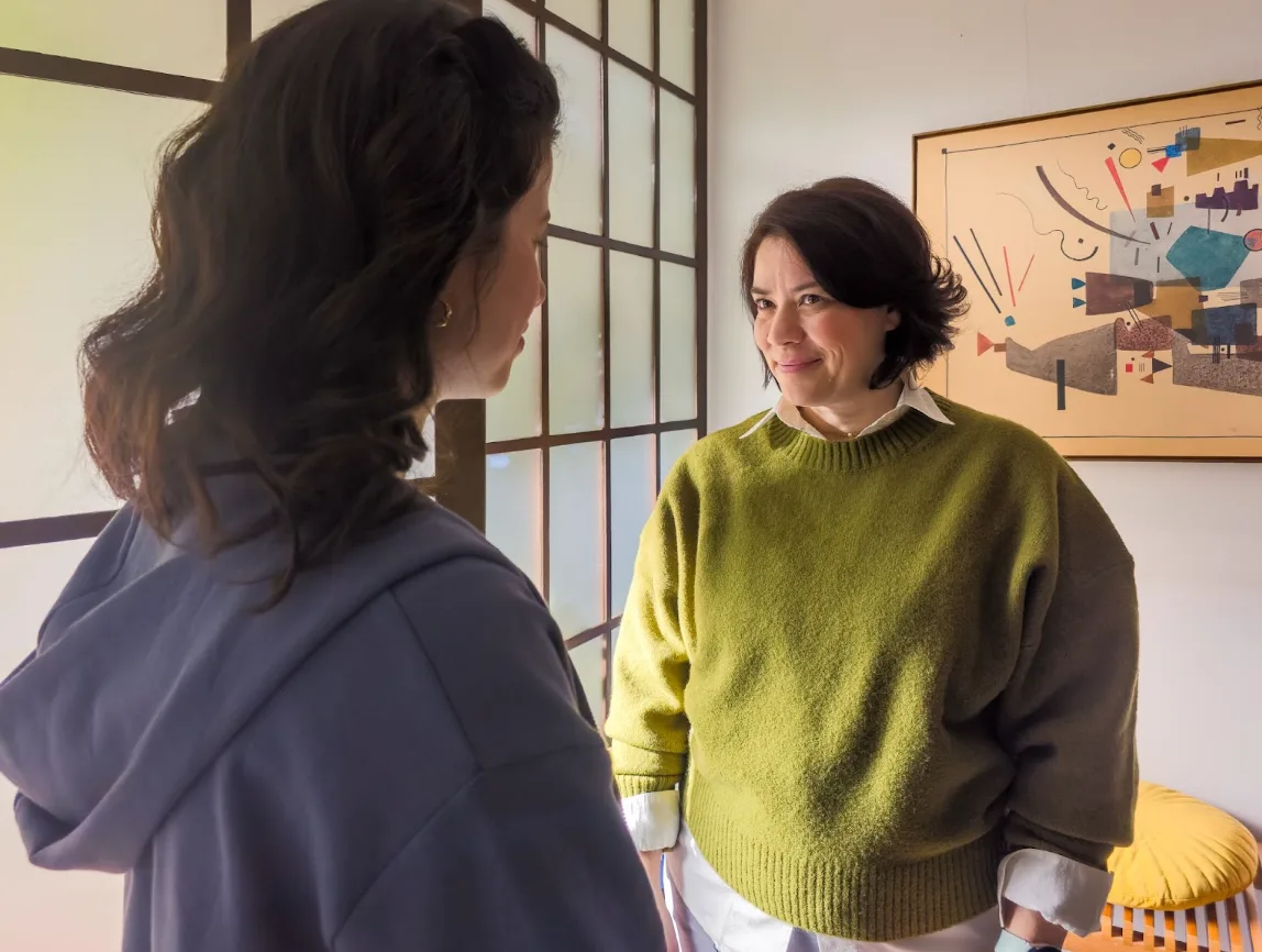 Duas mulheres conversando em sala iluminada.