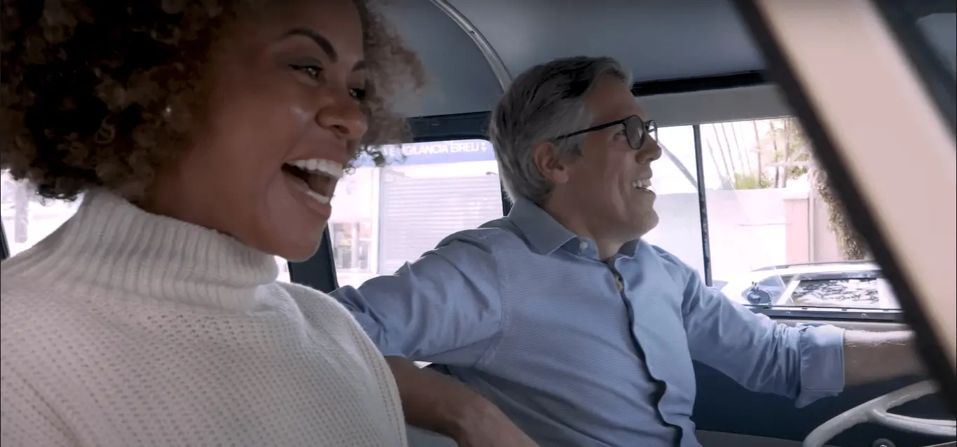 Casal sorrindo dentro de um carro antigo.