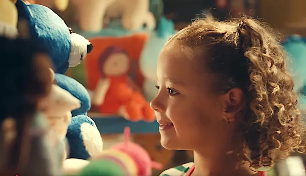 Criança sorrindo perto de pelúcias coloridas.