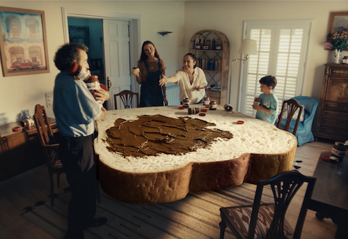 Pessoas ao redor de pão gigante na sala.