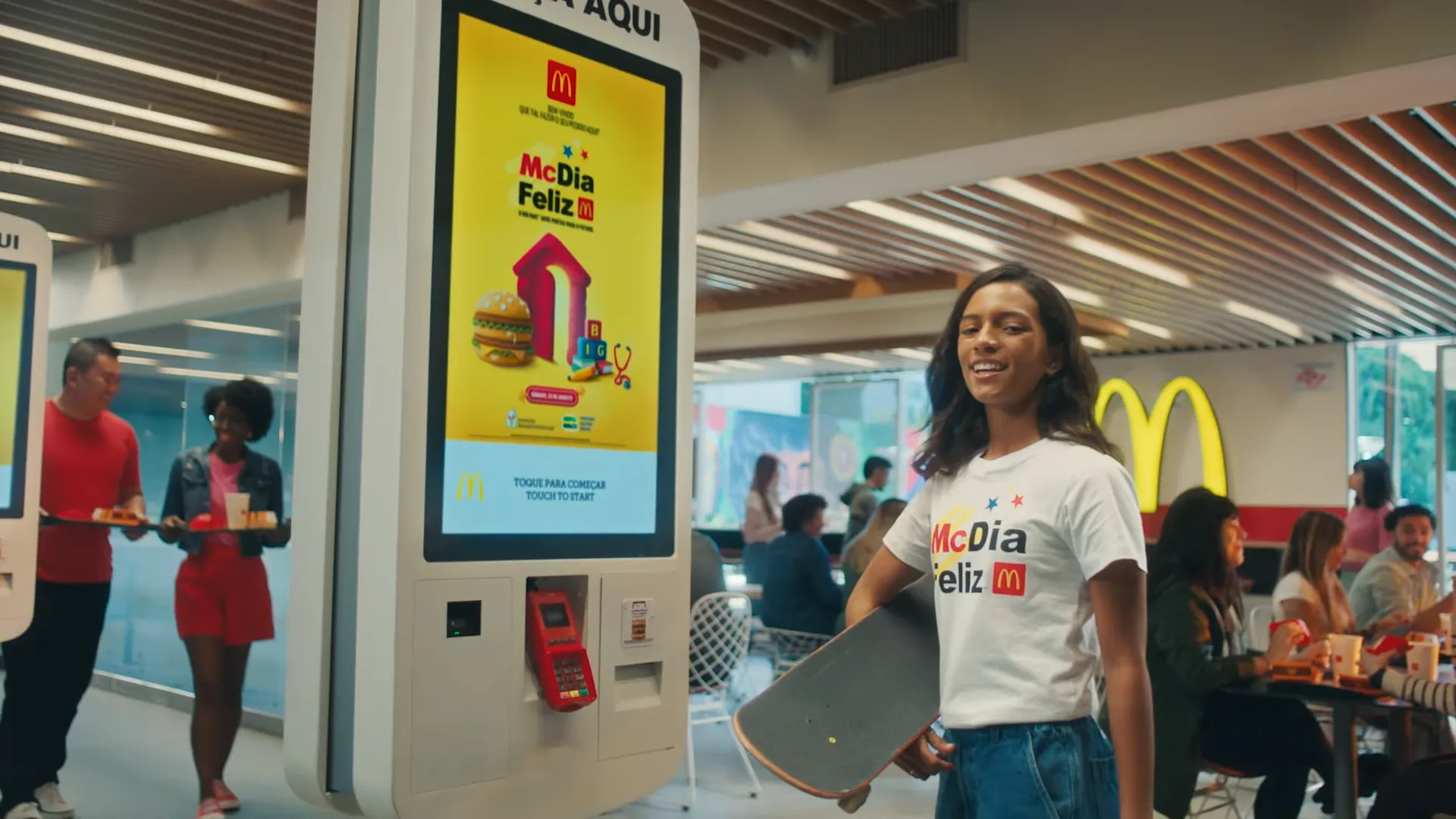 Mulher com skate, quiosque McDonald's ao fundo.