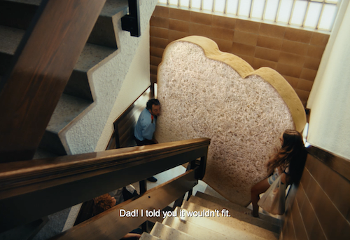 Pessoas carregando sofá gigante em formato de pão.